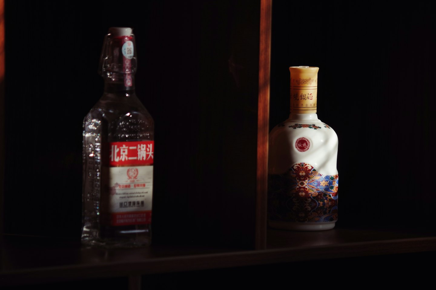 Two spirits bottles sit together on a wooden shelf.