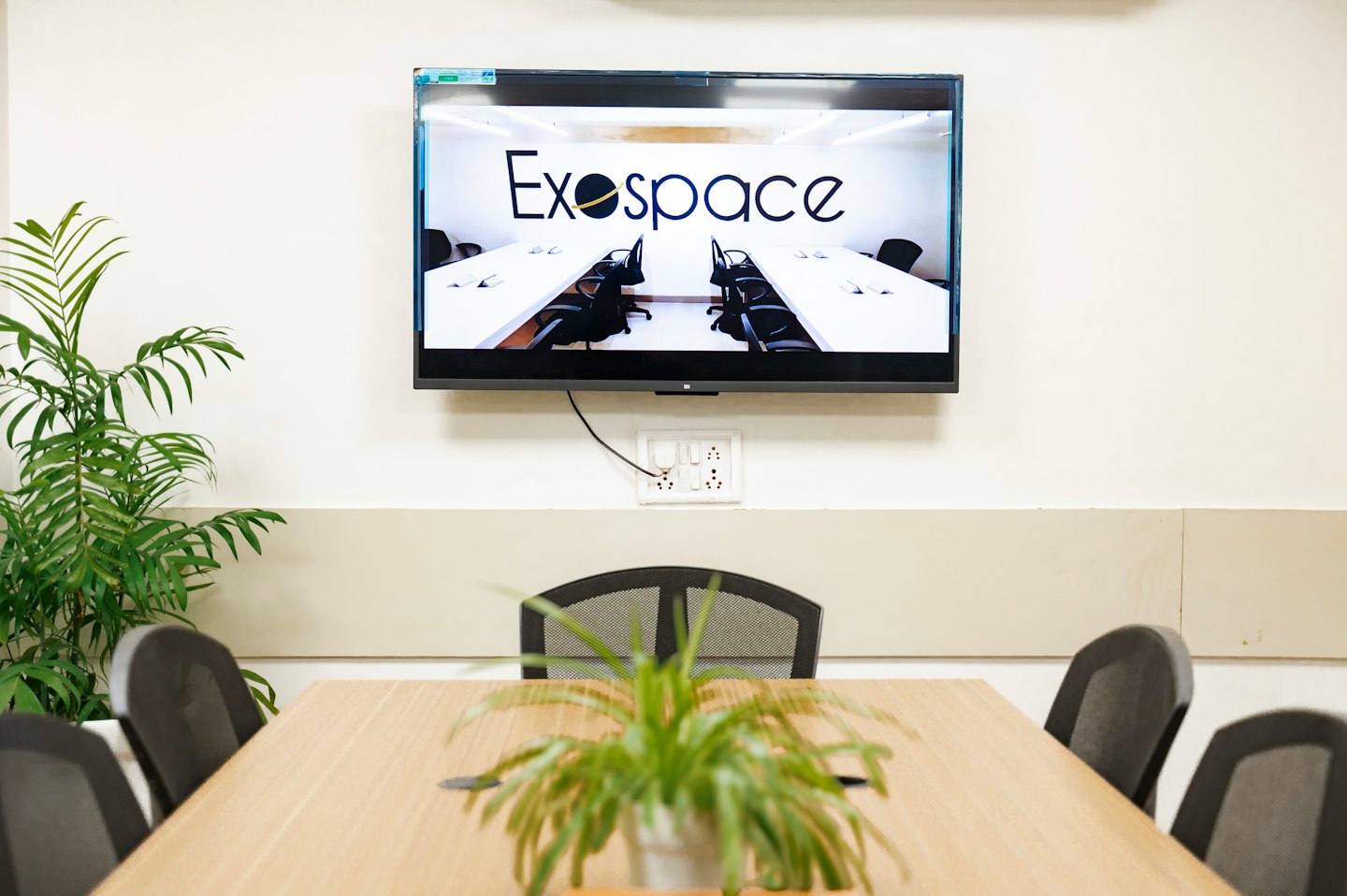 Corporate meeting room with a wooden table and wall monitor.