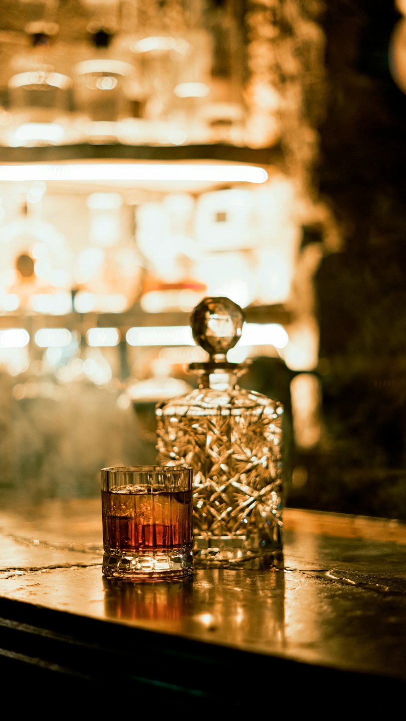 Amber whiskey in a glass with ice on a wooden bar.