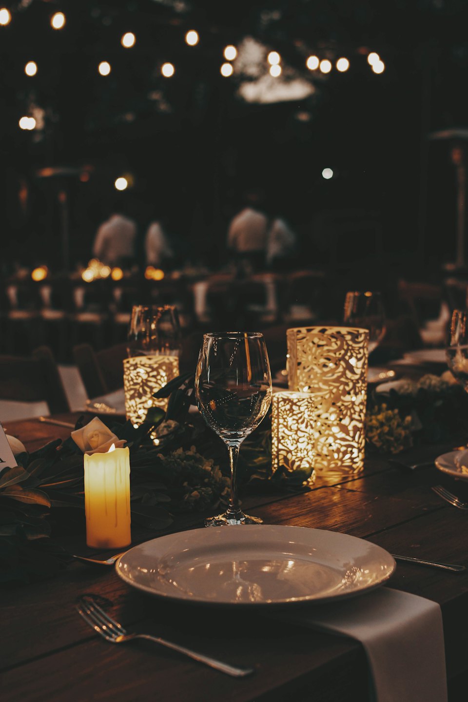 Wooden table set with dinnerware, wine glass, and candle for an event.